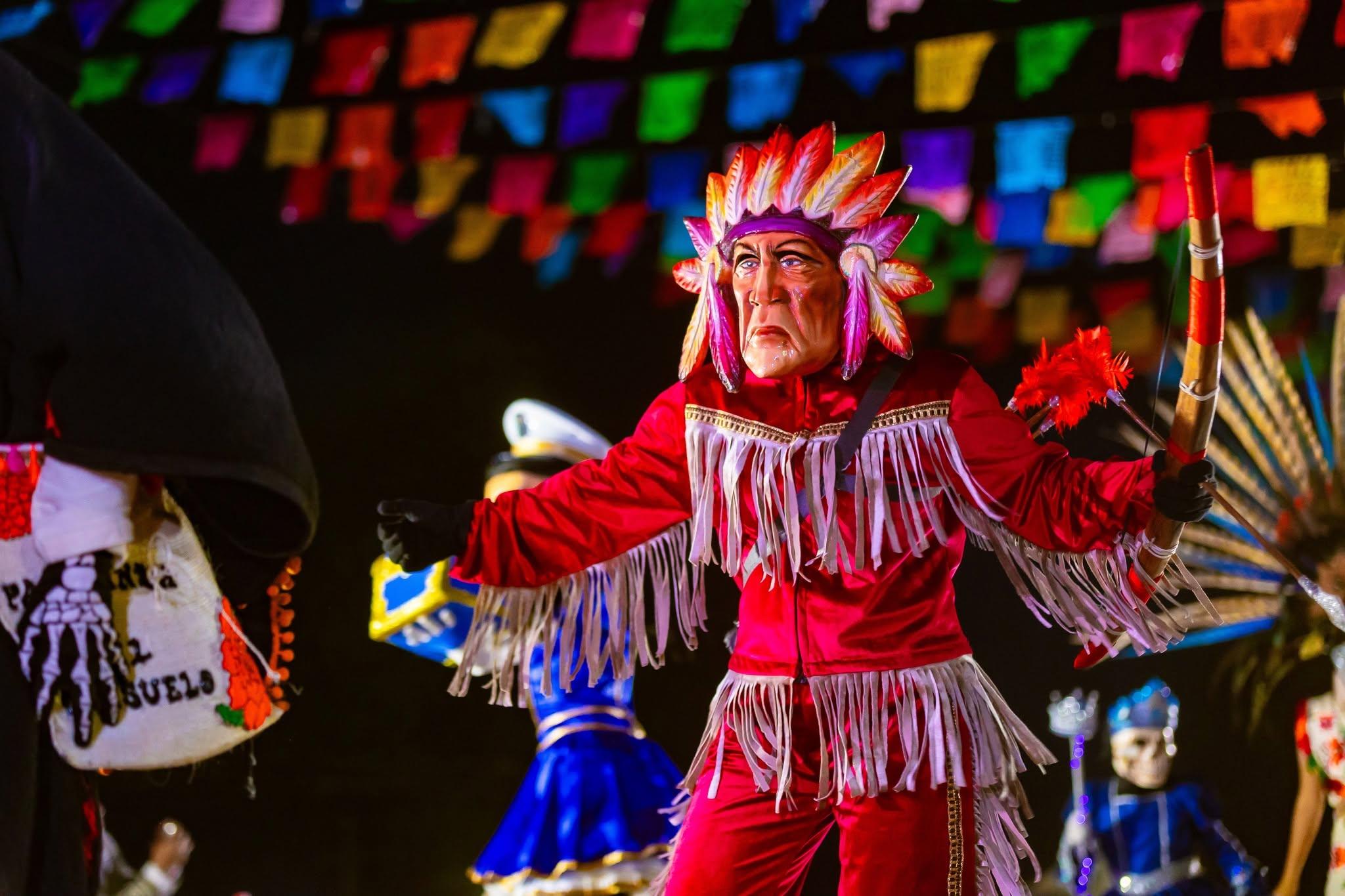 Comancha con penacho de plumas y vestido rojo danzando en el Xantolo